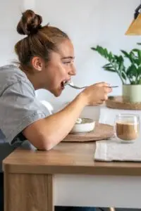 Mujer sentada en una mesa comiendo de un bol con una cuchara representando la ventana de alimentación en el ayuno intermitente