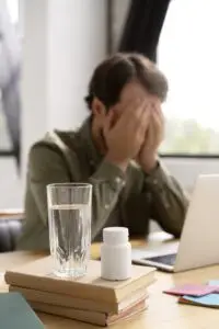 Persona sentada en un escritorio con la cabeza entre las manos, mostrando signos de fatiga o dolor de cabeza, posibles efectos secundarios al comenzar el ayuno.