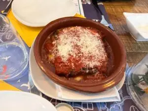 Parmigiana di Melanzane servida en cuenco de barro con queso rallado.